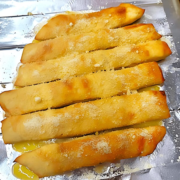 Golden-brown Momo's Pizzeria breadsticks, topped with parmesan cheese, on a foil-lined baking sheet.