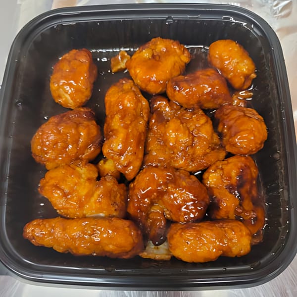 A black container filled with Momo's Pizzeria's boneless chicken wings, coated in a glistening orange sauce.