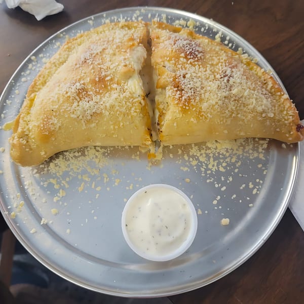 A golden-brown calzone, cut in half and sprinkled with cheese, served with a side of dipping sauce.