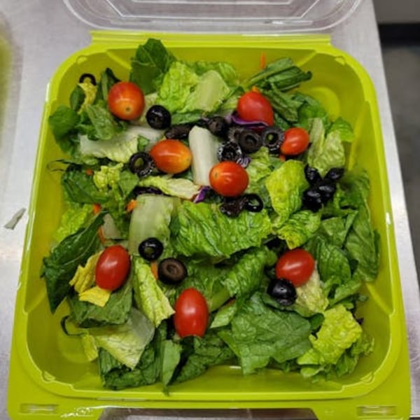 Fresh green salad with cherry tomatoes and black olives in a lime green container.